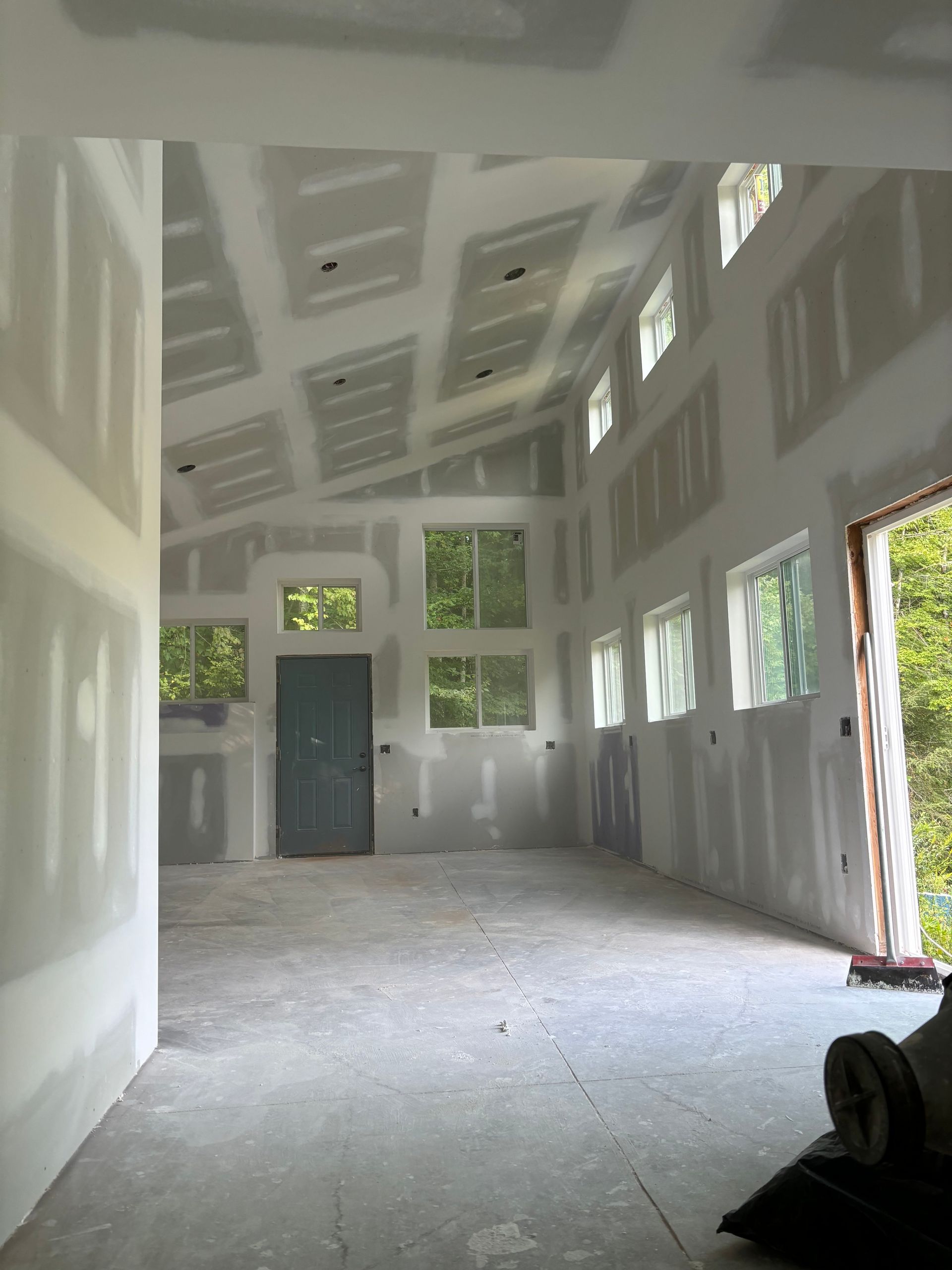 Empty unfinished room with high white ceilings, gray walls, and daylight from many windows.