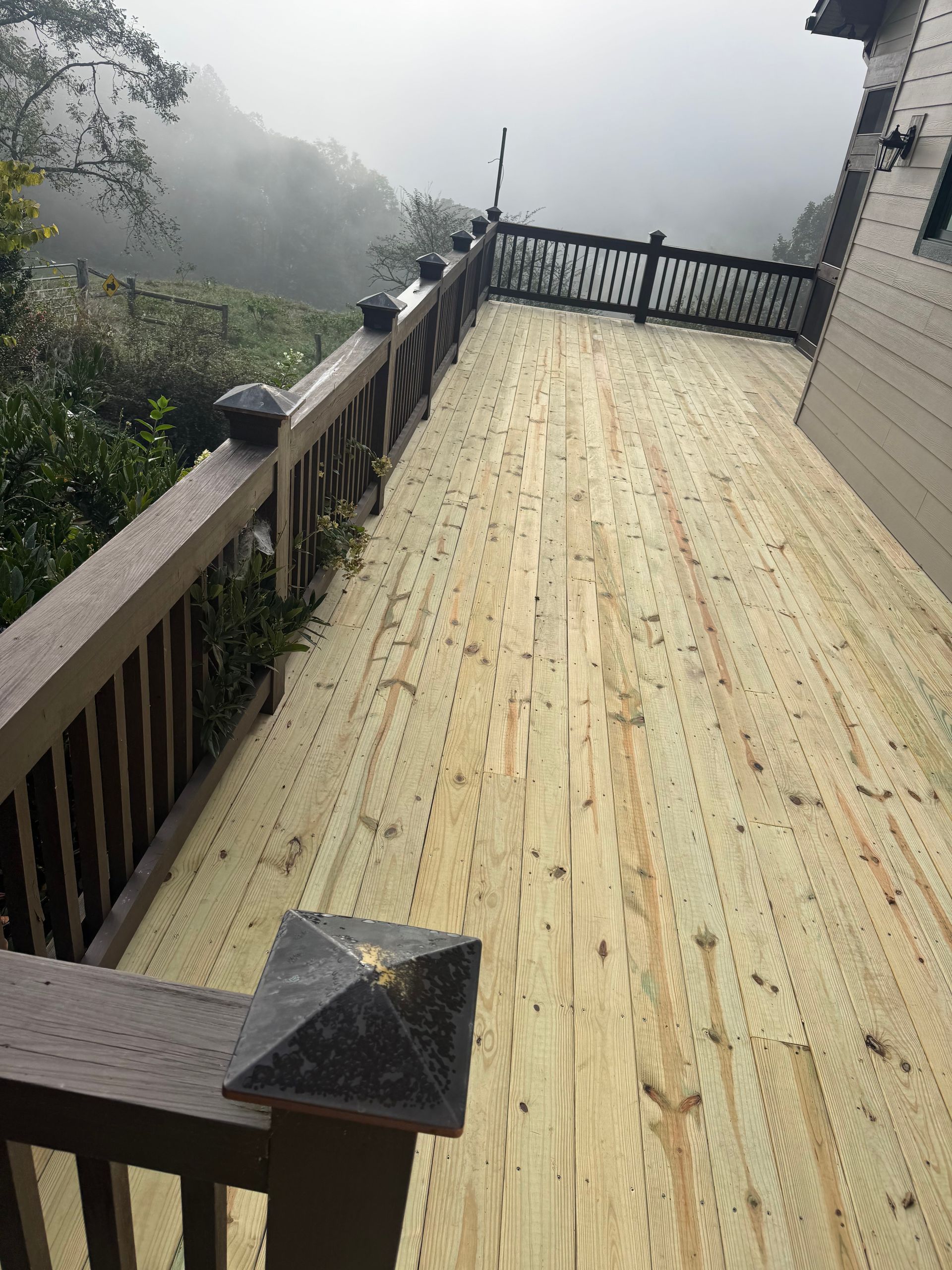 Foggy wooden deck with railing and decorative posts overlooking a misty landscape
