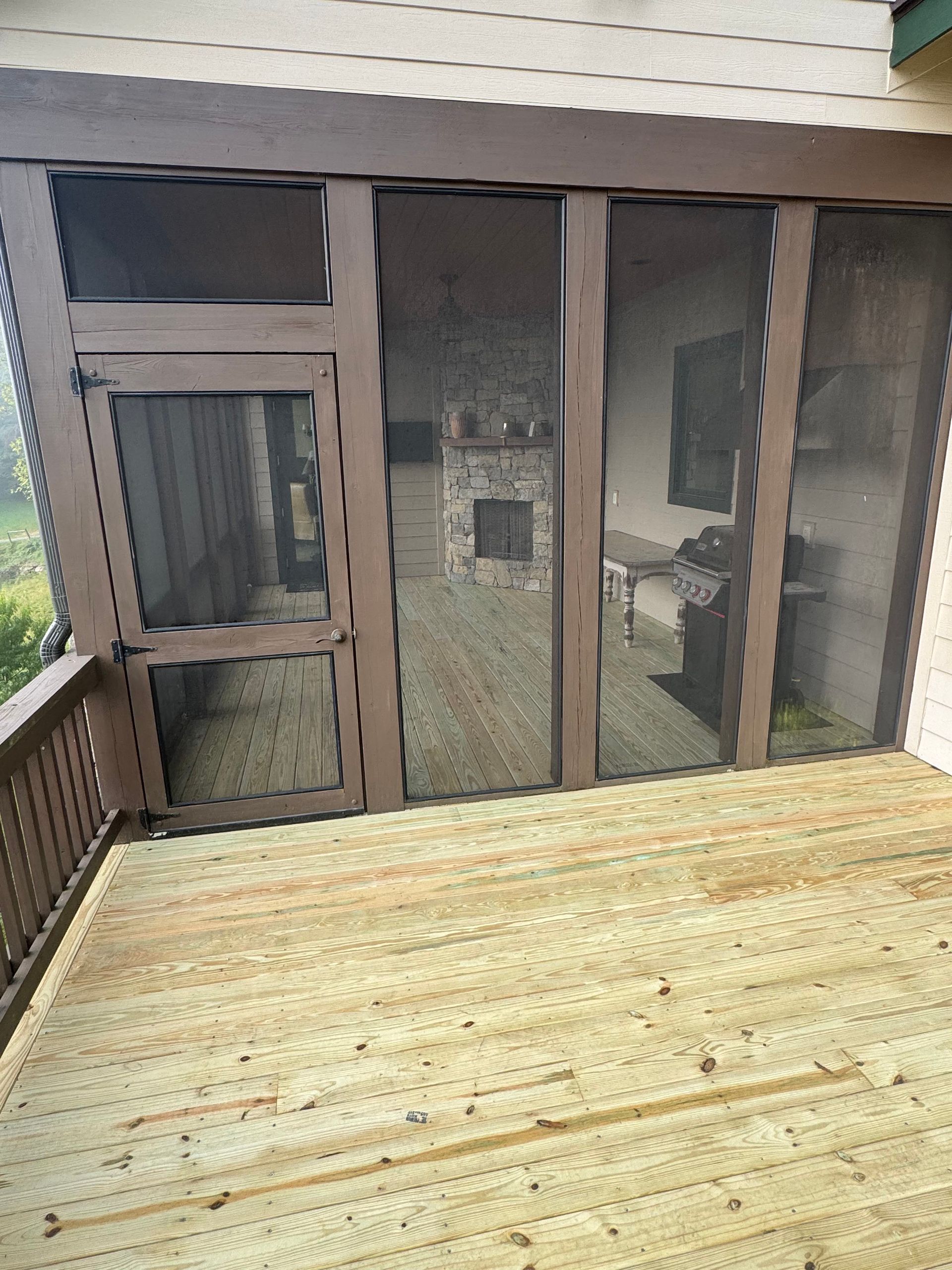 Wooden deck facing a screened porch with sliding glass doors and a small side window.