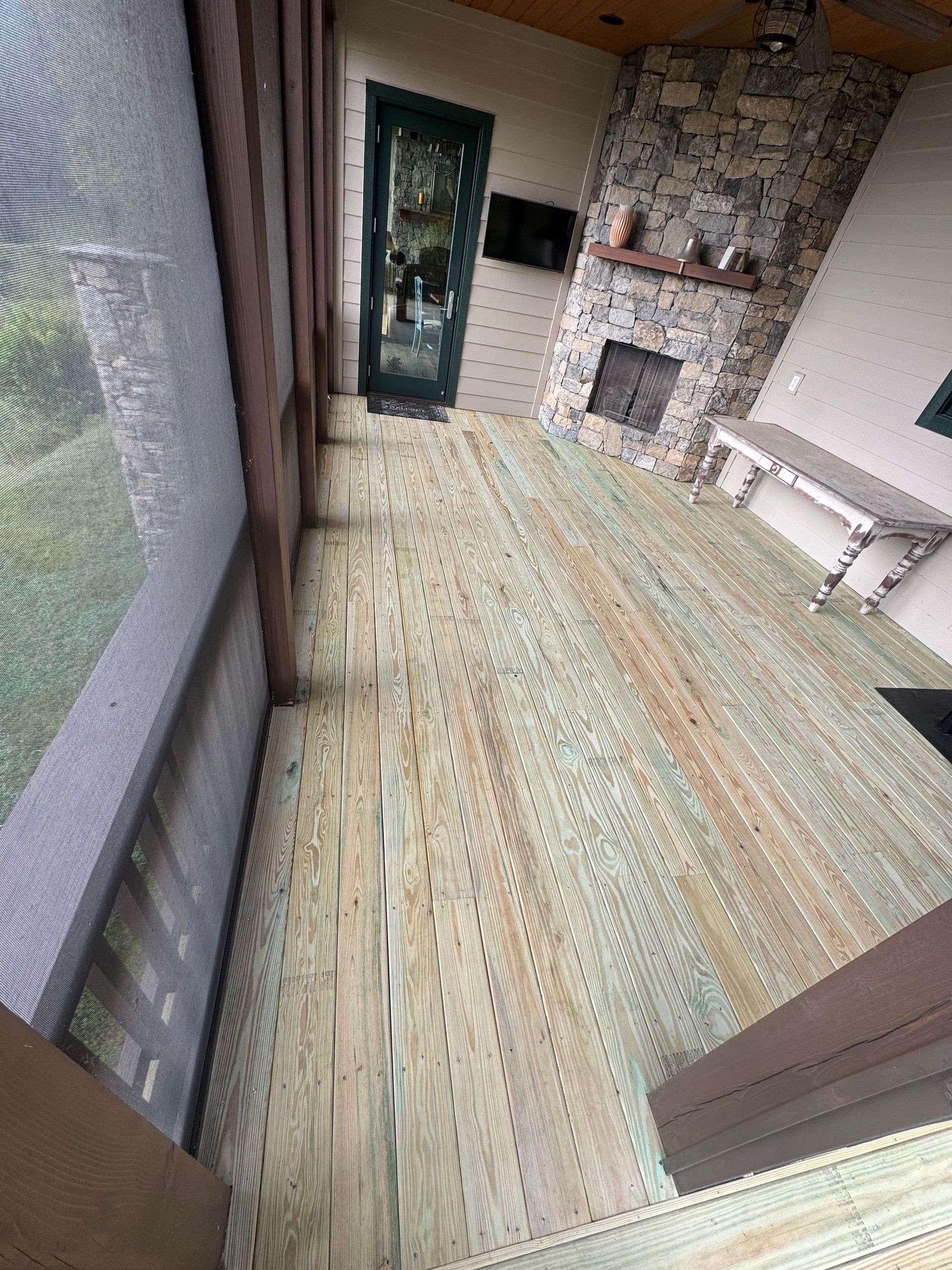 Slanted view of a rustic living room with a stone fireplace, green rug, and white side table
