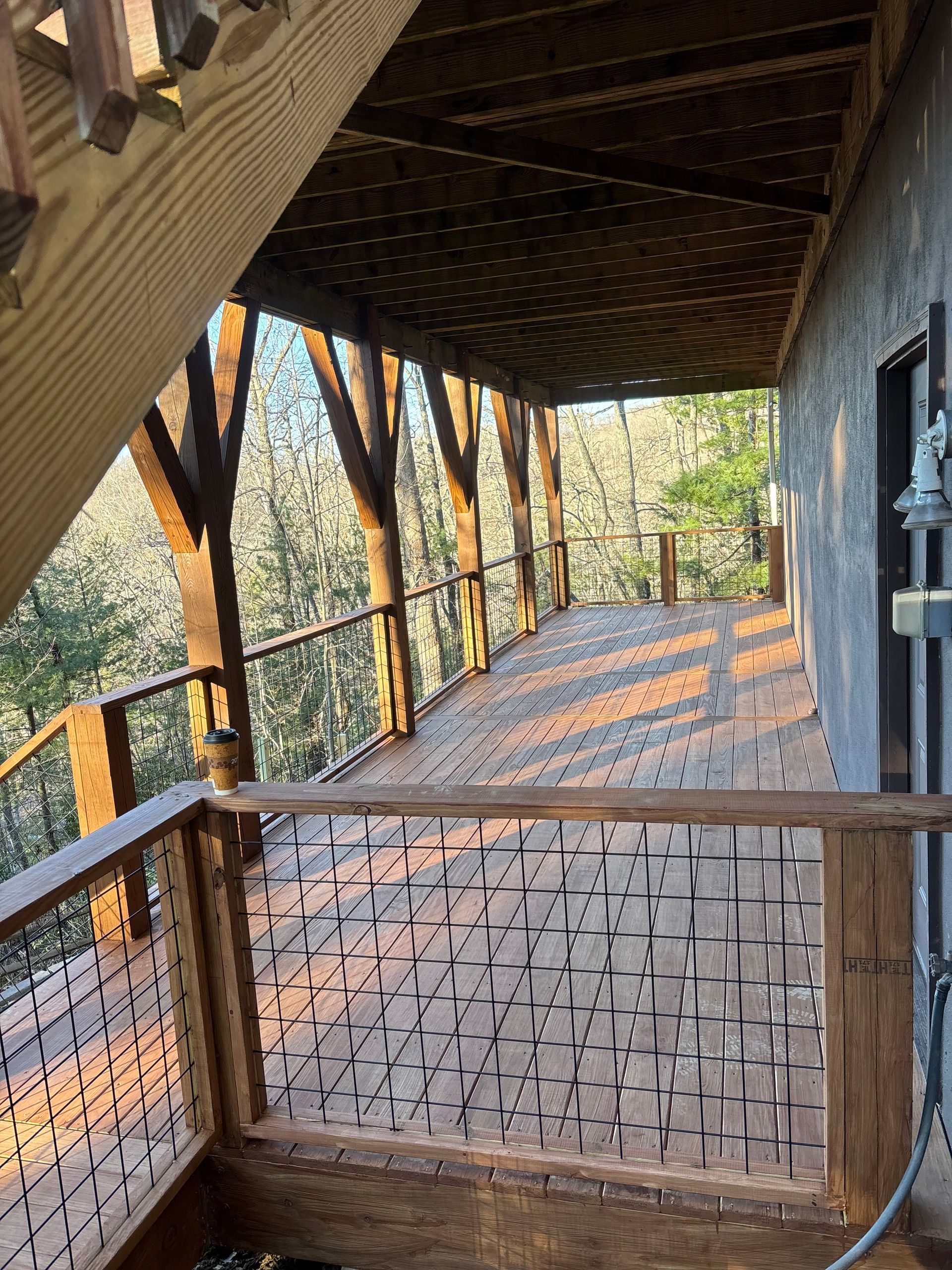 Covered wooden porch overlooking a sloped walkway with railings and autumn trees beyond.