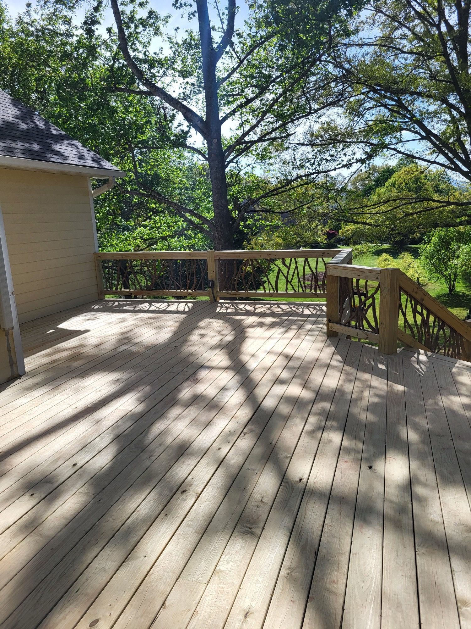 Wooden deck with railing, overlooking trees in bright sunlight.