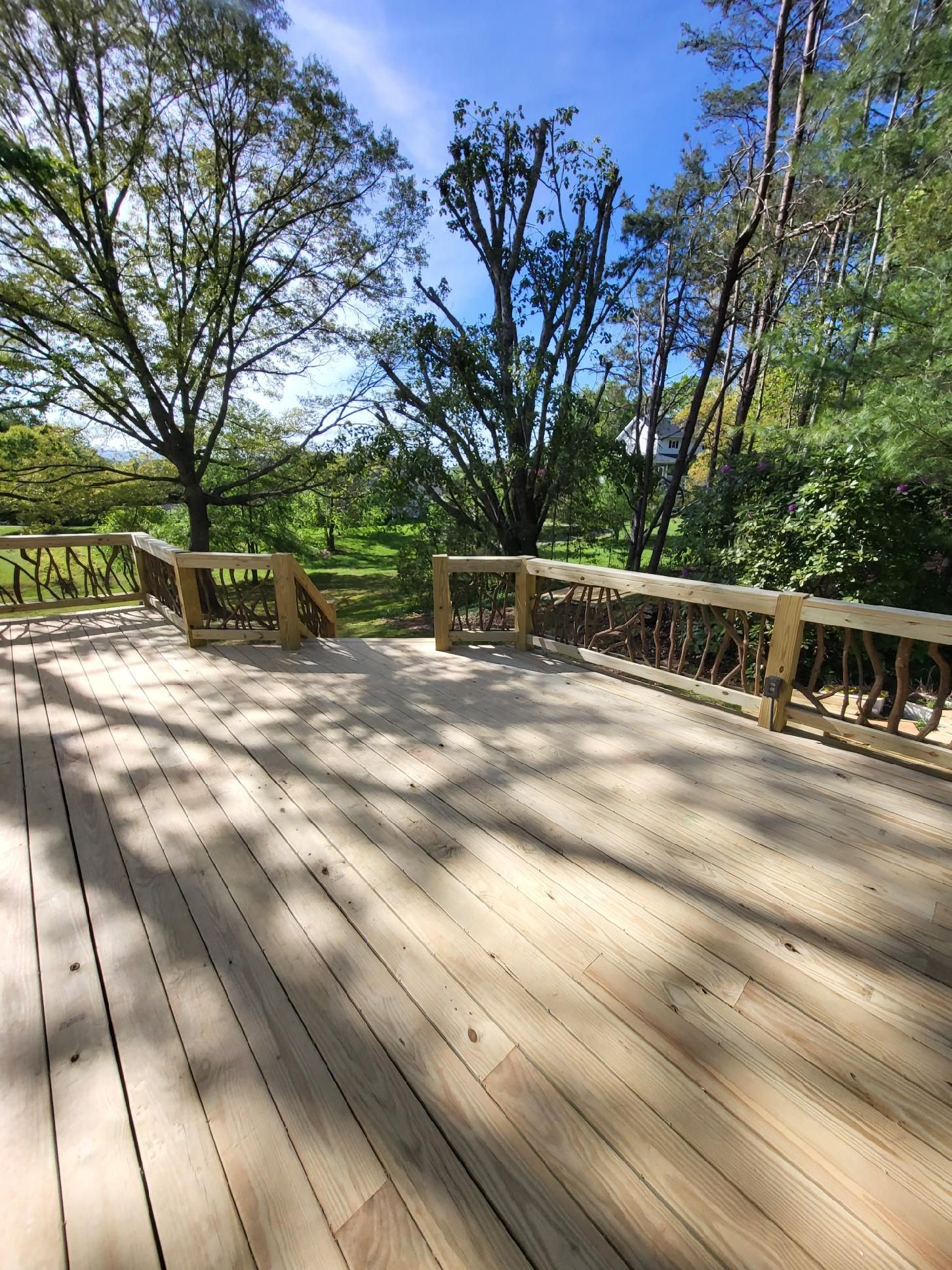 Wooden deck with railing overlooking leafy trees on a sunny day