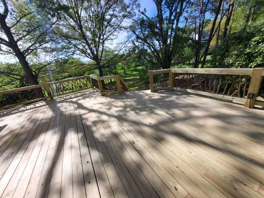 Wooden deck overlook with railings, surrounded by trees and bright sunlight casting shadows