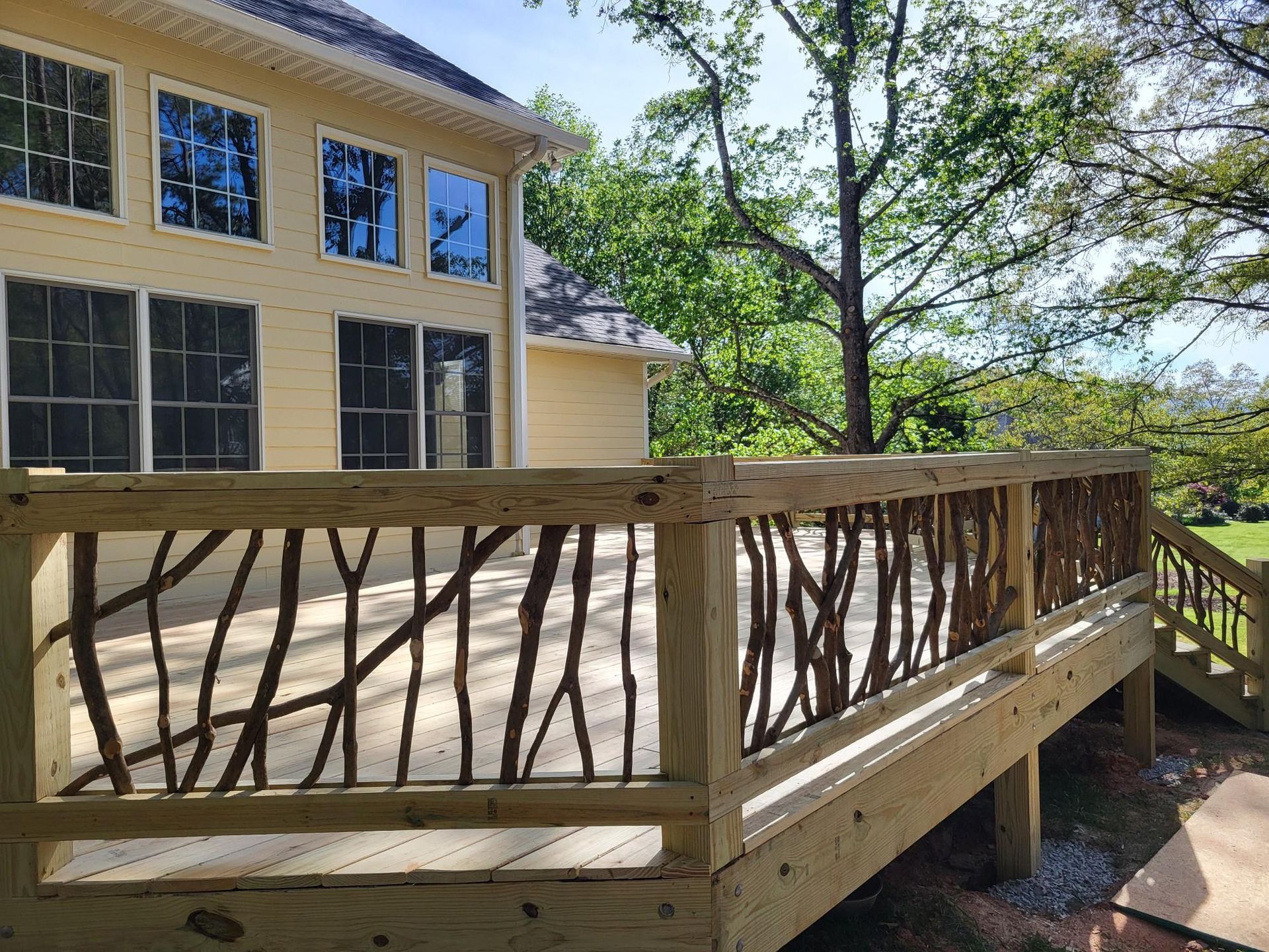 Wooden deck railing beside a yellow house with large windows and trees in the background