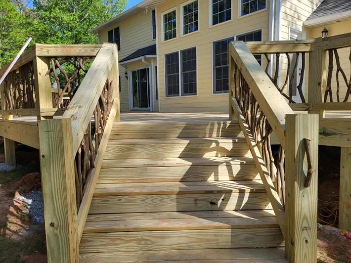 Wooden ramp leading to a yellow house with steps and railings, surrounded by trees