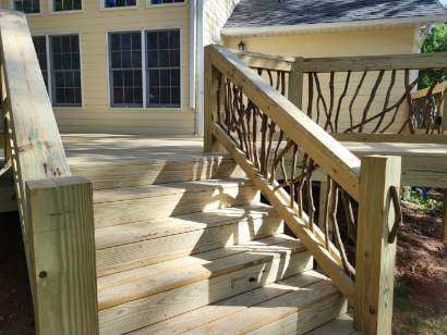 Wooden staircase and railing leading to a house deck beside large windows