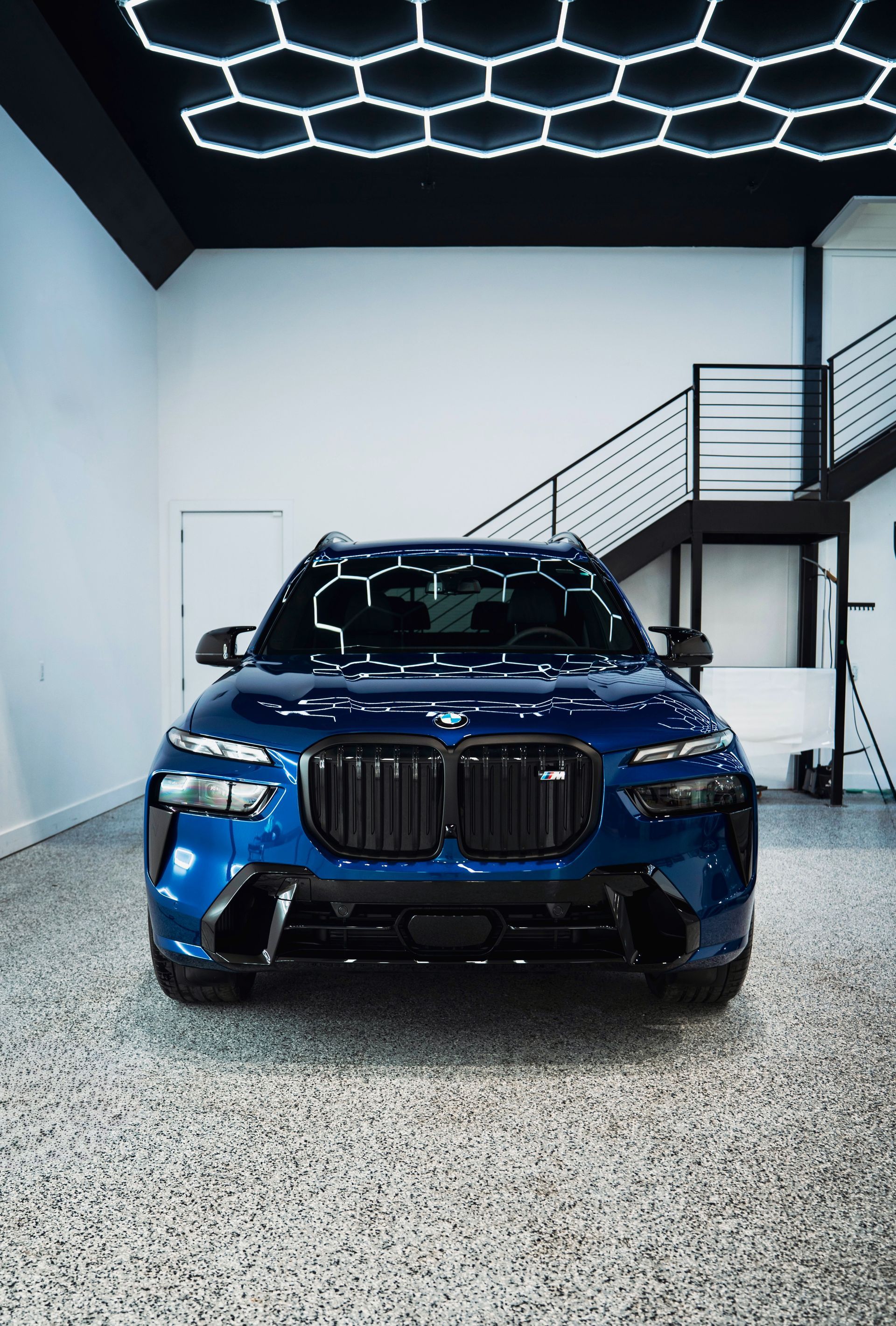 Blue BMW SUV in a modern showroom with a hexagon-lit ceiling and staircase in the background