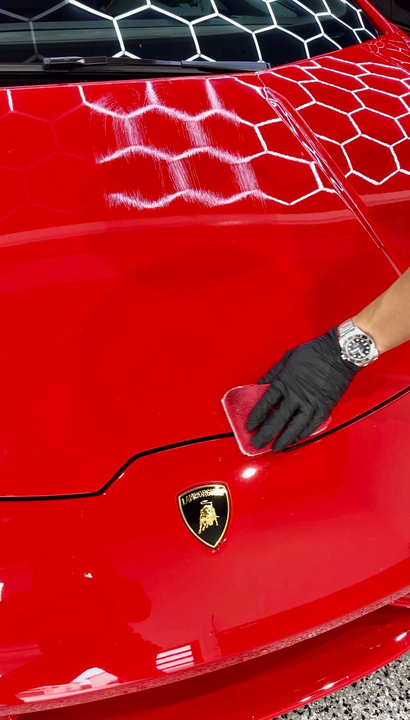 A person wearing gloves uses an applicator pad to apply a coating to the hood of a red lamborghini huracan lp610-4.