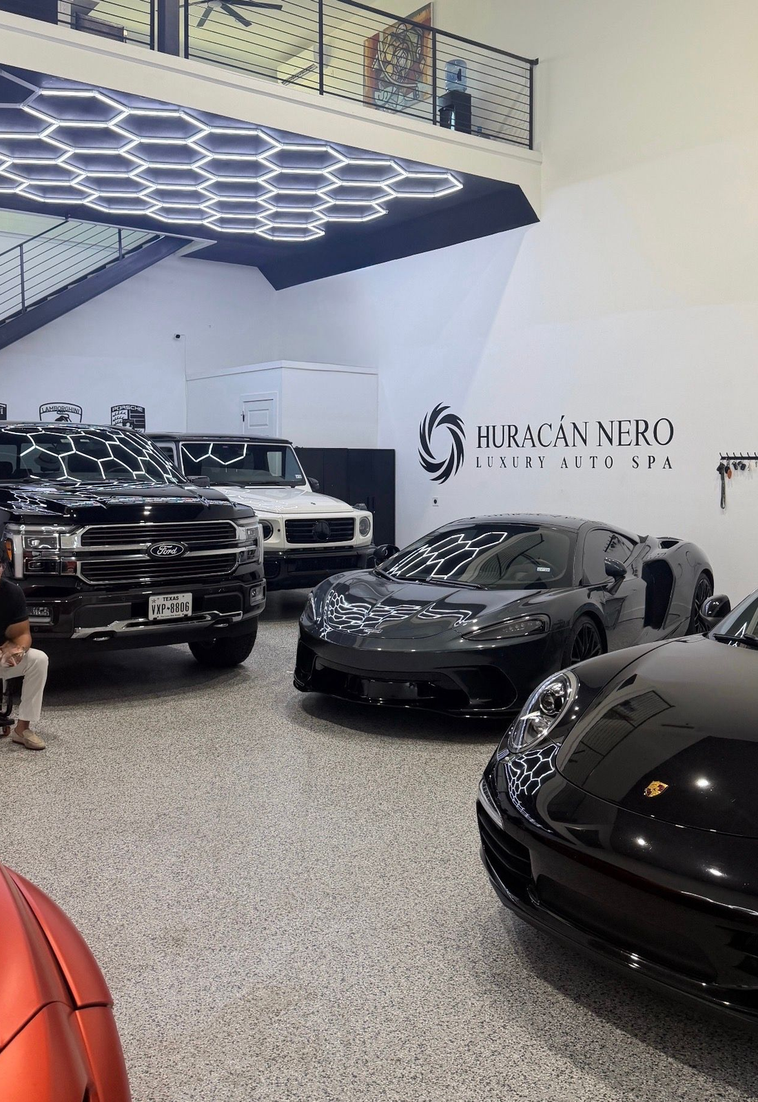 Luxury car showroom with several black sports cars under bright geometric ceiling lights
