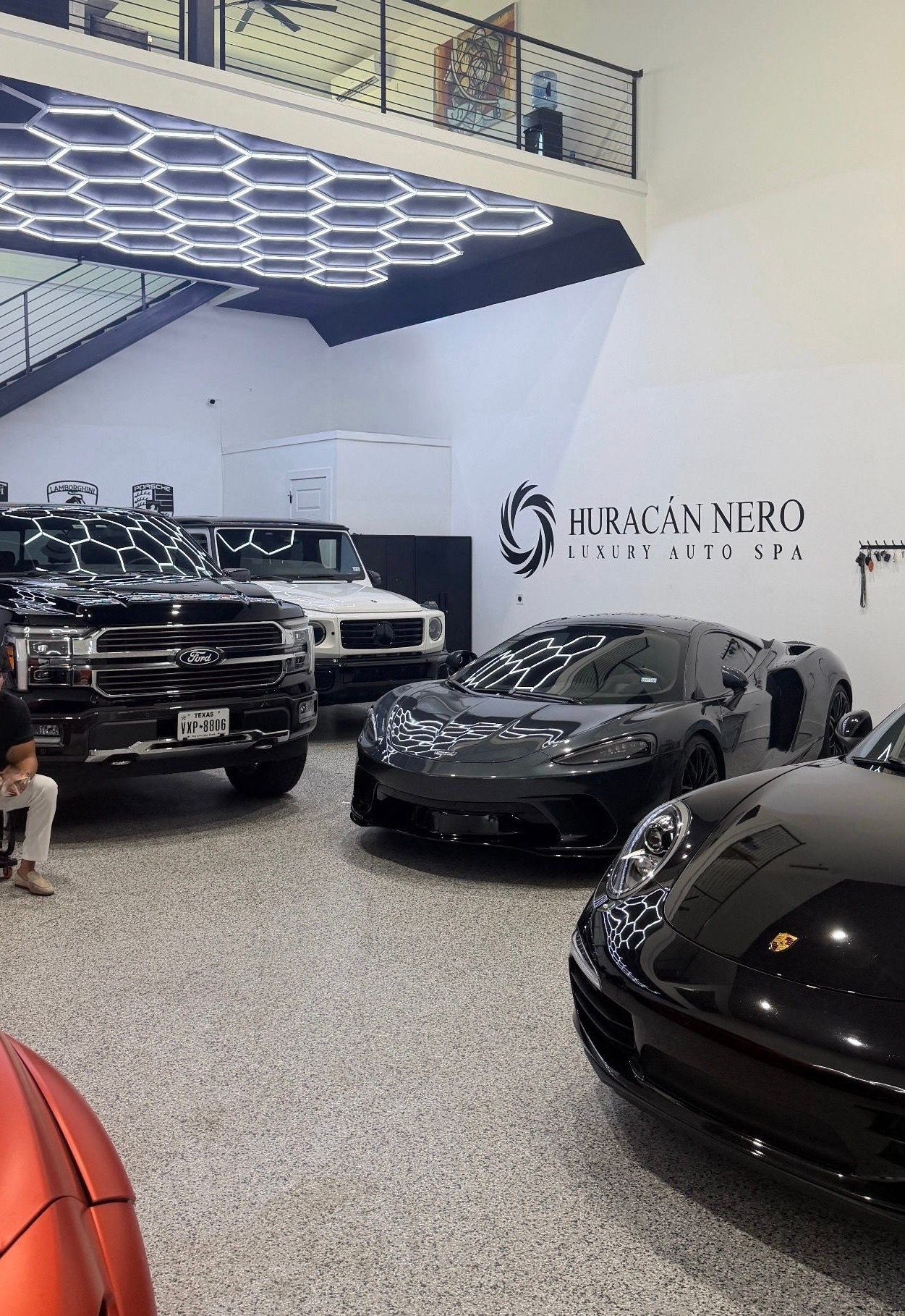 Luxury car showroom with several black sports cars under bright geometric ceiling lights
