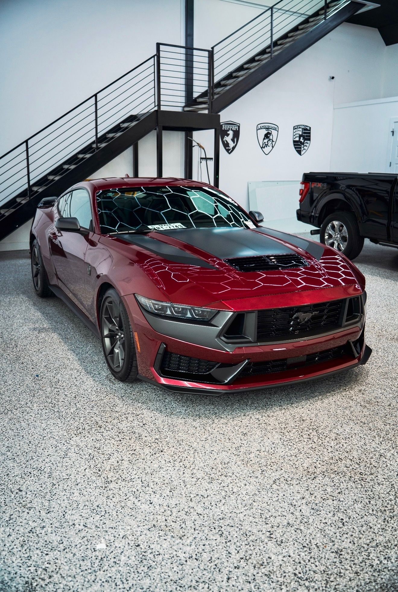 Red sports car in a modern garage with a staircase and black SUV in the background