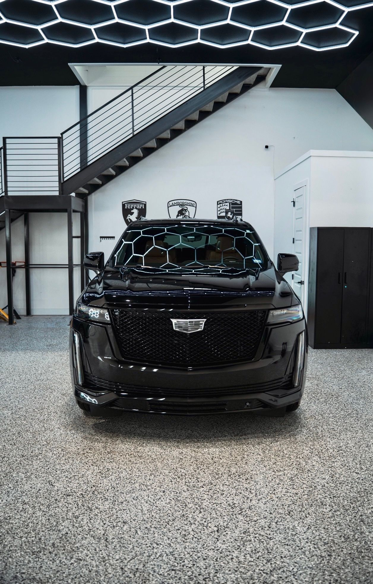 Black SUV parked in a modern garage with a staircase and hexagonal ceiling lights