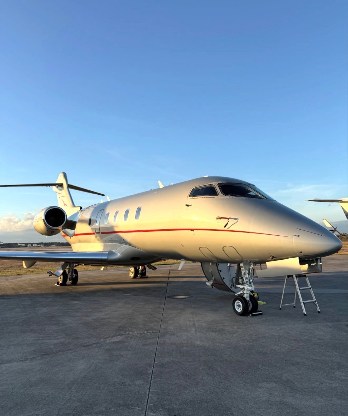 Small private jet on an airport tarmac at sunset, with stairs at the front and a clear blue sky.