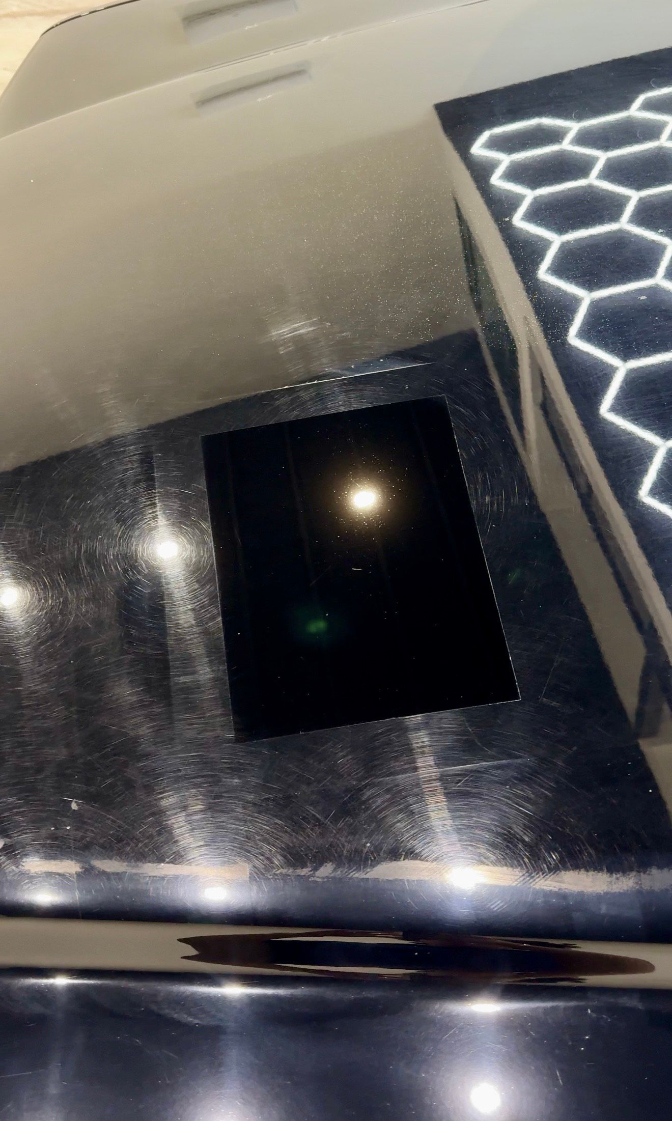 Bright light reflecting off a shiny, dark surface; close-up with a honeycomb-patterned light.