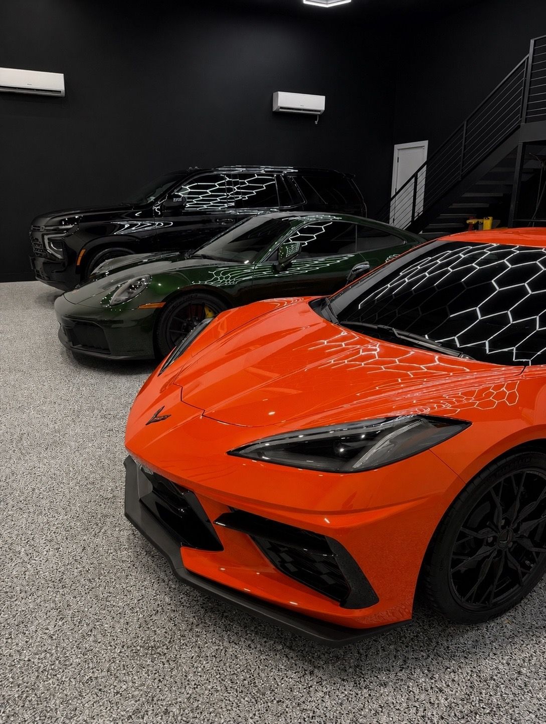 Orange sports car in a showroom, with black and dark green cars behind it.