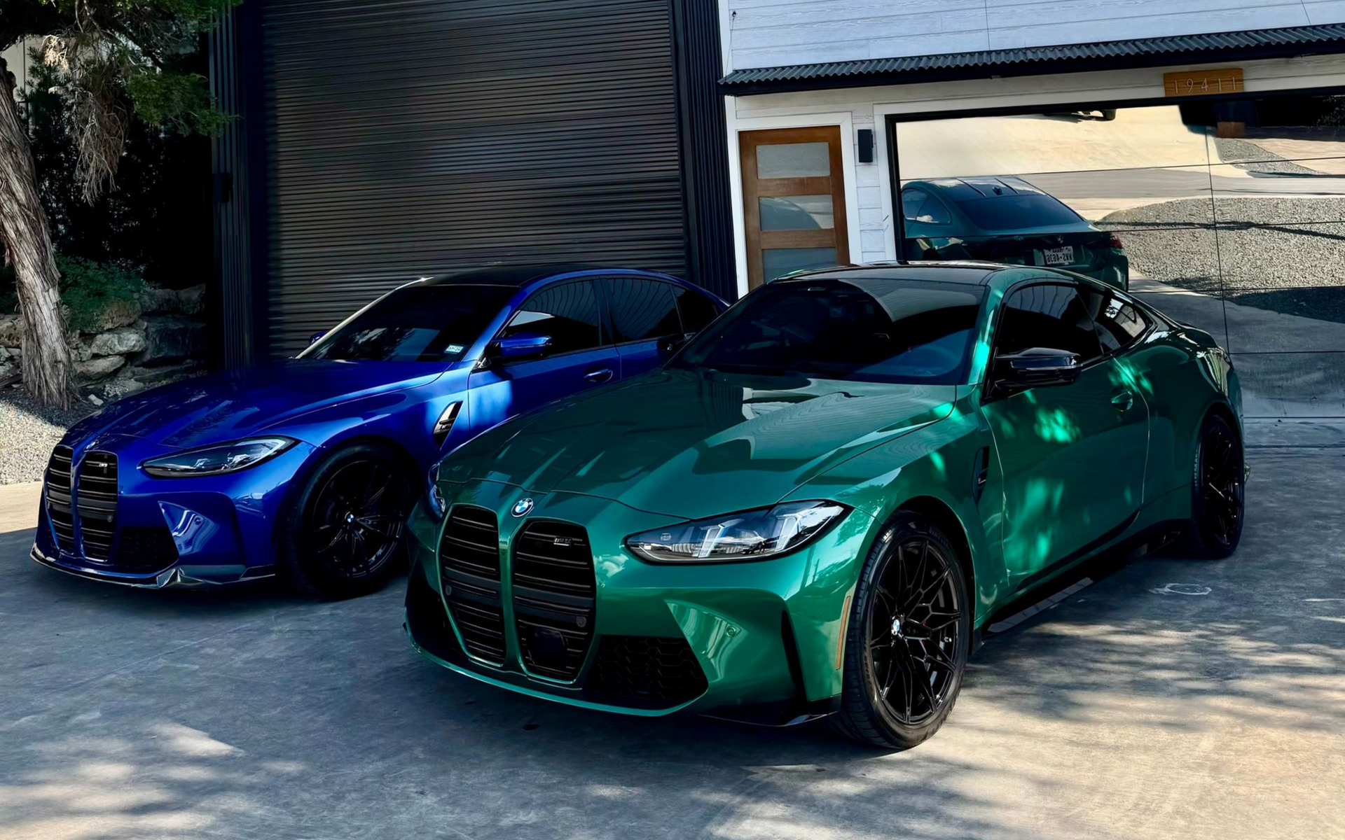 Two sporty sedans, one blue and one green, parked side by side in a driveway.