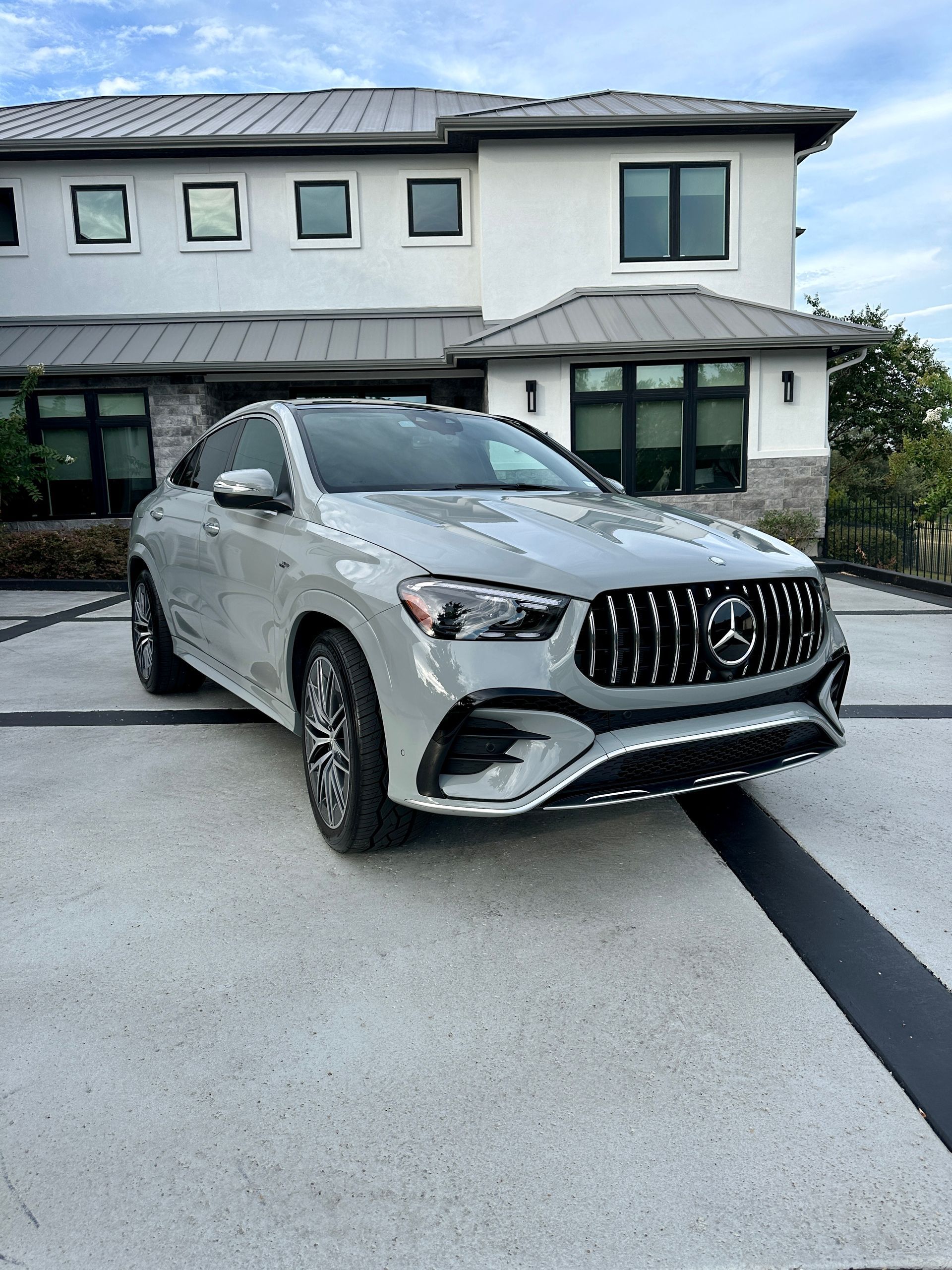 Gray Mercedes-Benz SUV parked on a concrete driveway in front of a modern white house with dark trim.