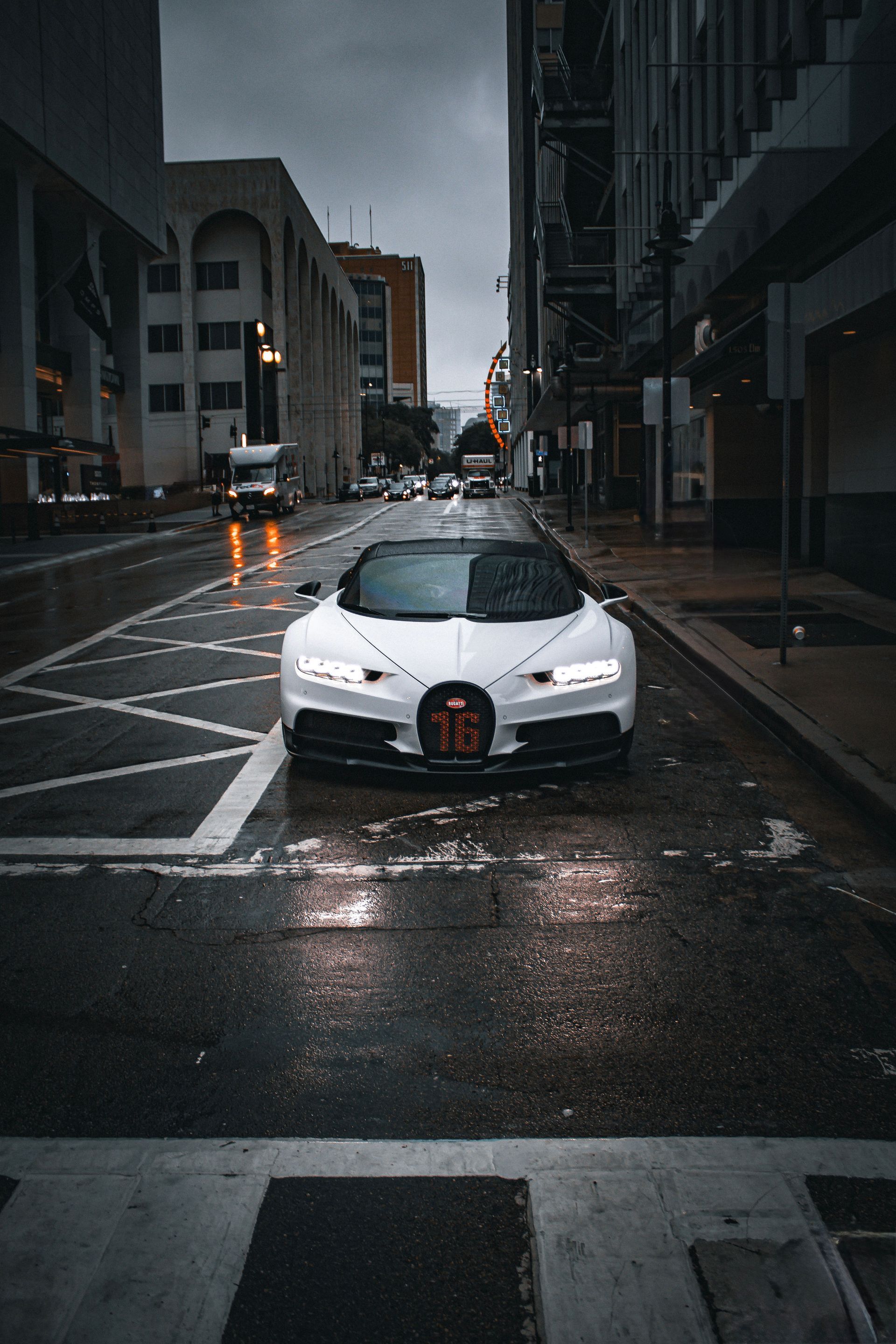 White sports car parked on a wet city street between tall buildings at dusk