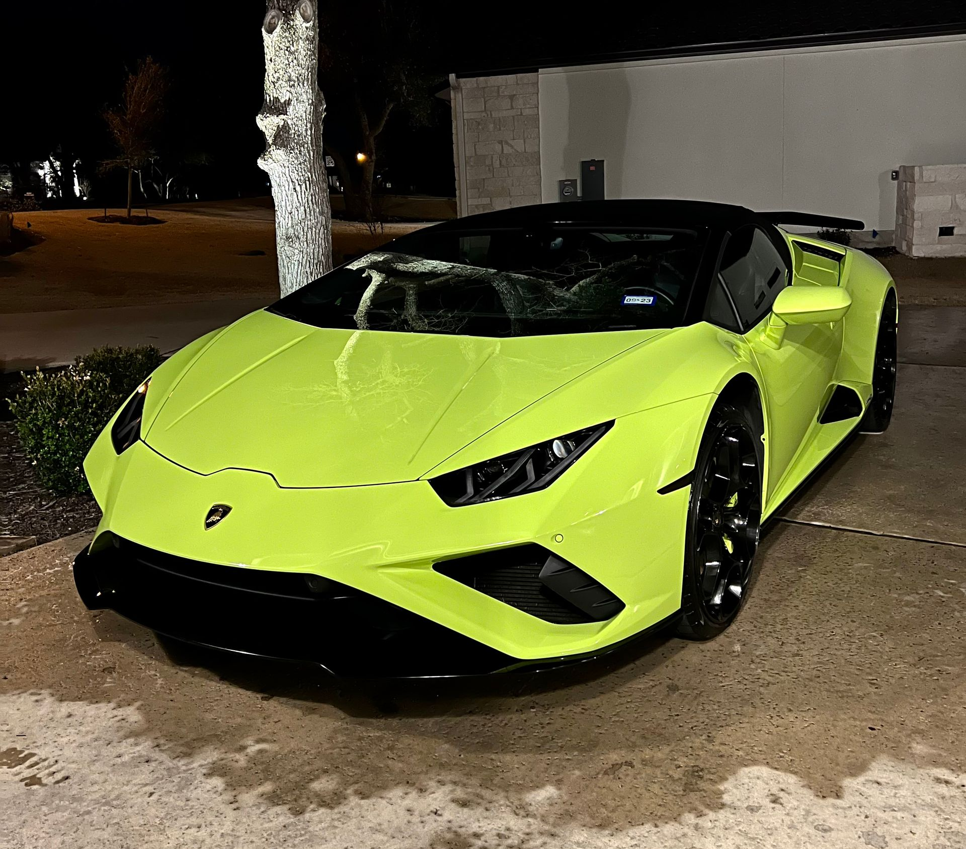 Neon green Lamborghini sports car parked at night on a driveway near a wall and tree.