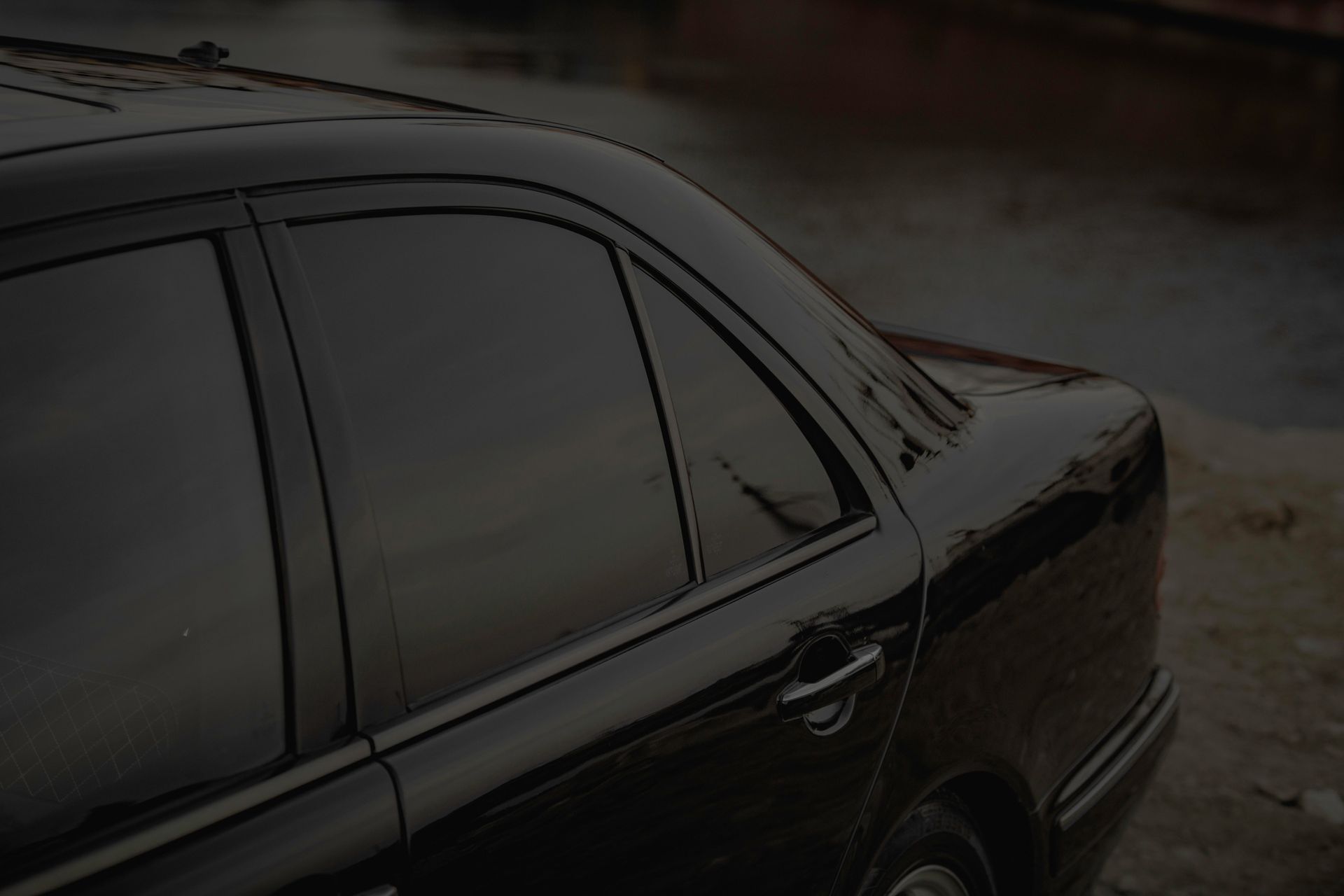 Dark sedan parked on a wet roadside in low light