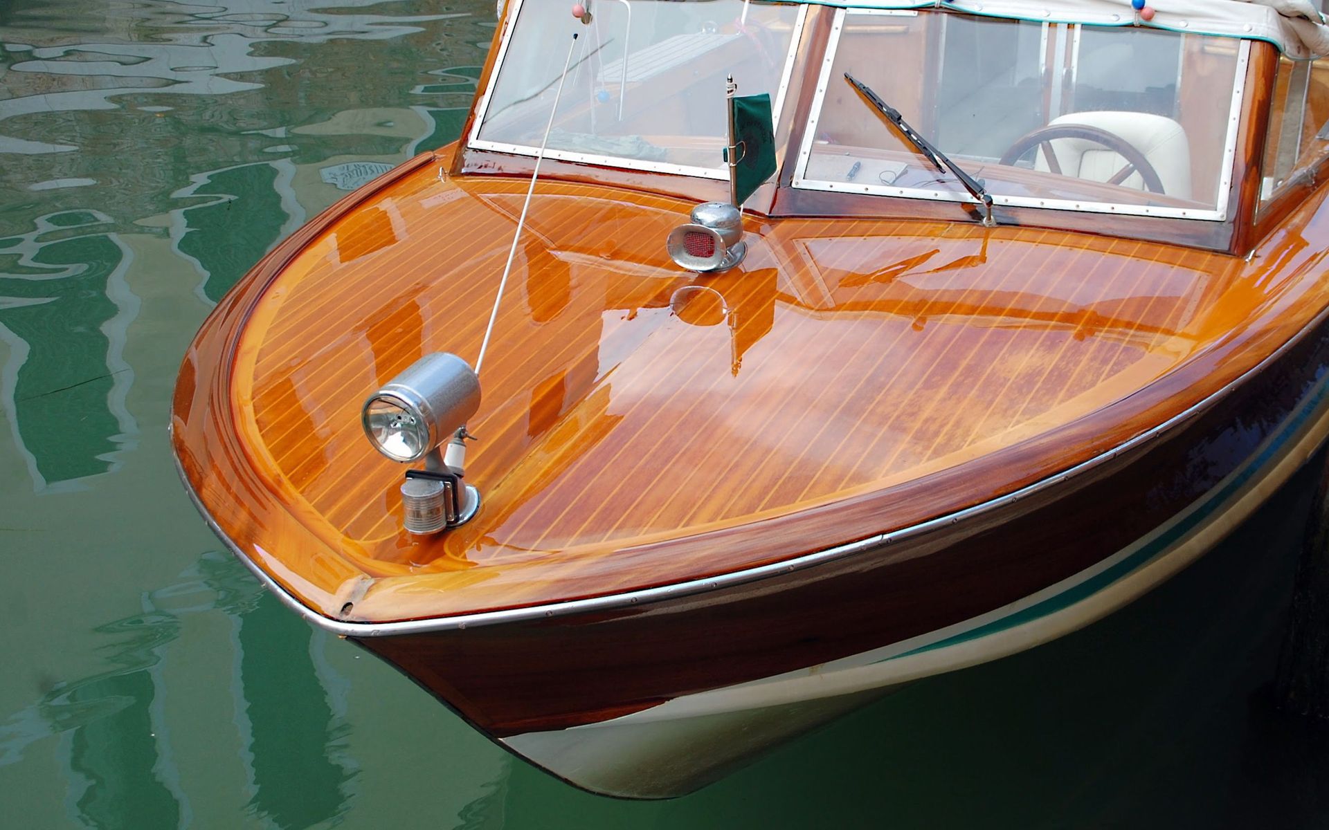 Wooden speedboat with polished orange deck floating on green water, front view