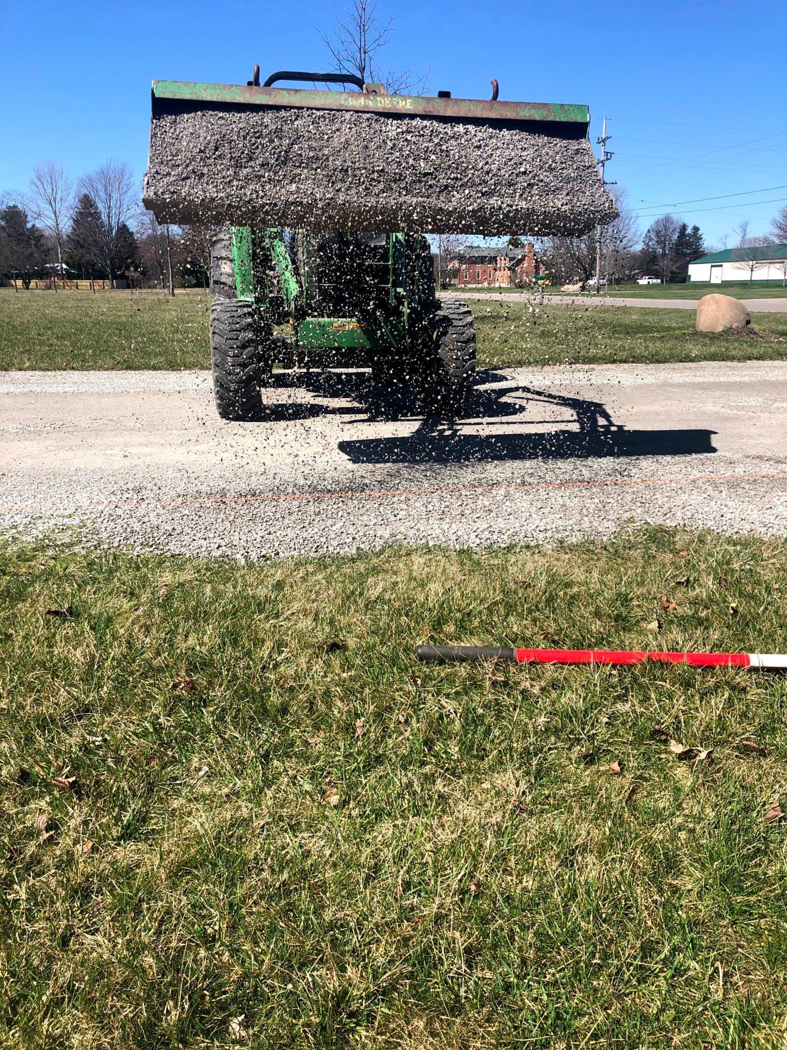 Green combine harvester throwing grain dust in a field under a clear blue sky
