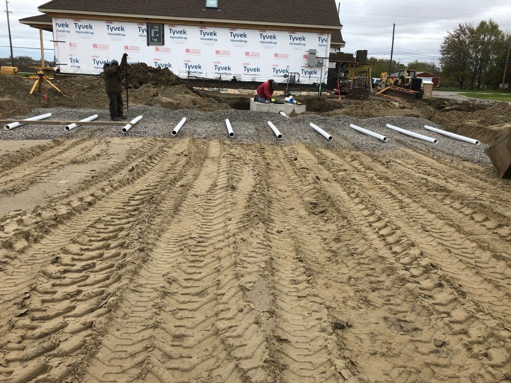 Muddy construction site with foundation trenches and a house under construction in the background