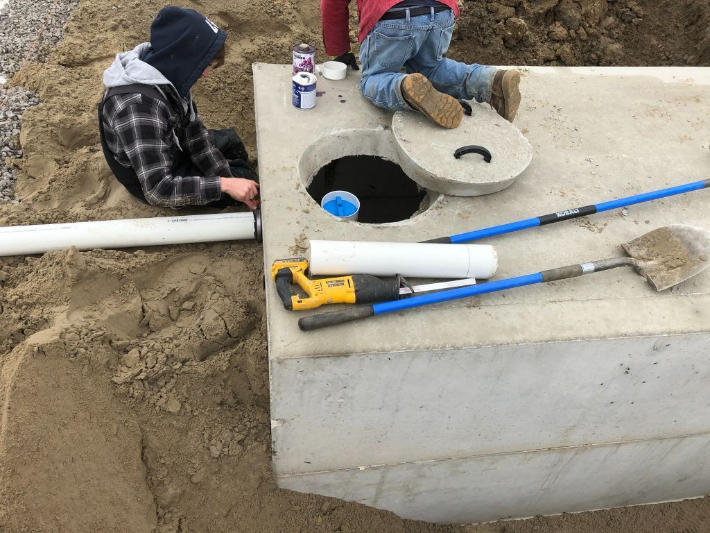 Construction workers installing underground utilities beside a concrete utility box with pipes and tools
