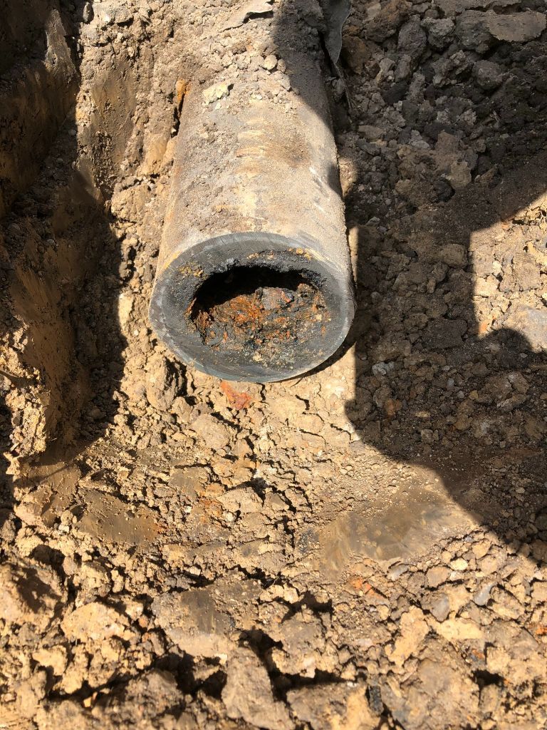 Rusty metal pipe protruding from cracked dirt in an excavation site