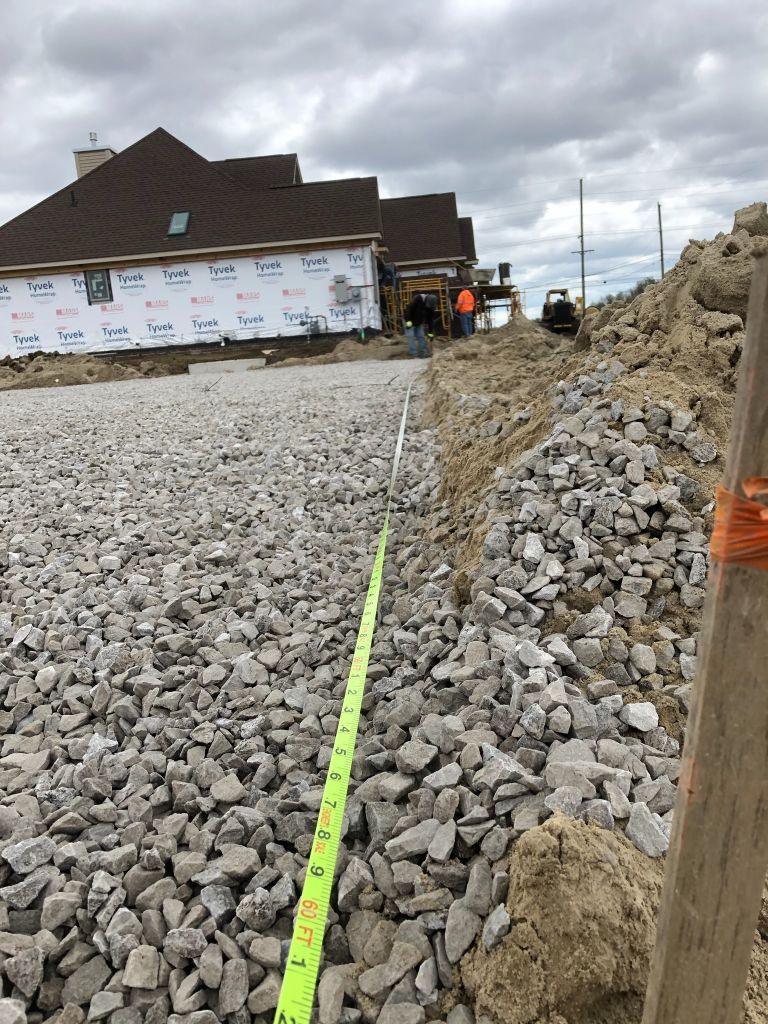 Construction site with gravel trench, measuring tape, and workers near a building under cloudy sky