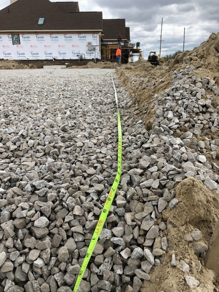 Construction site with gravel-covered slope, neon green hose, and workers near a house under renovation