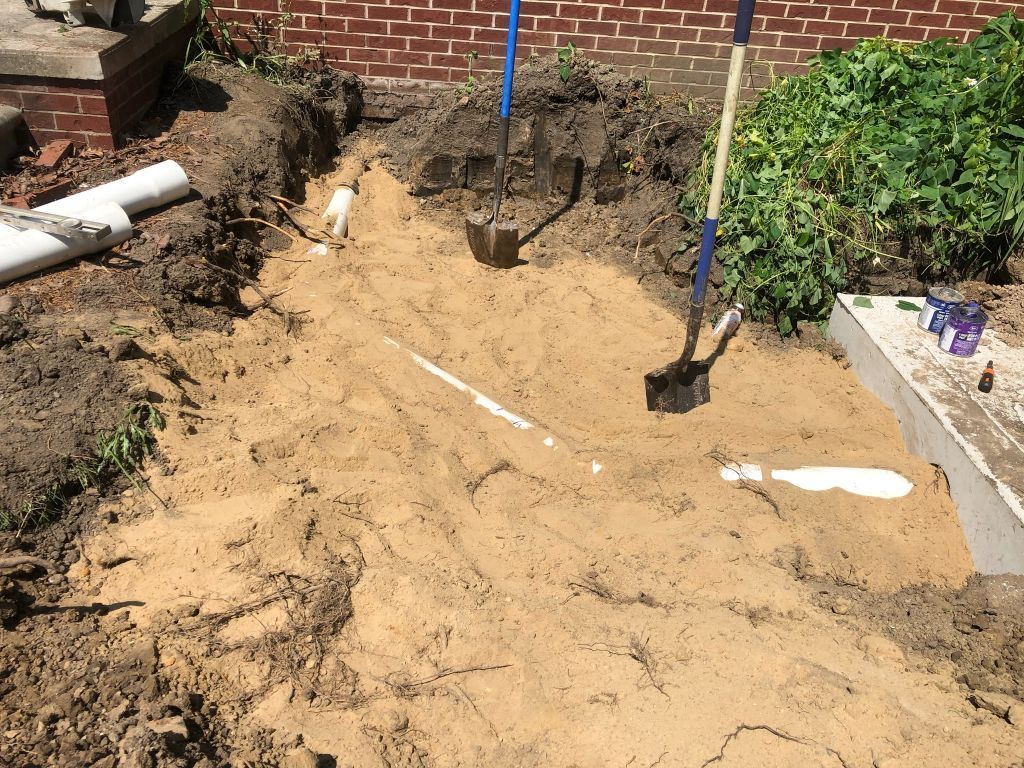 Backyard excavation with a sandy dirt pit, shovel, and brick wall border