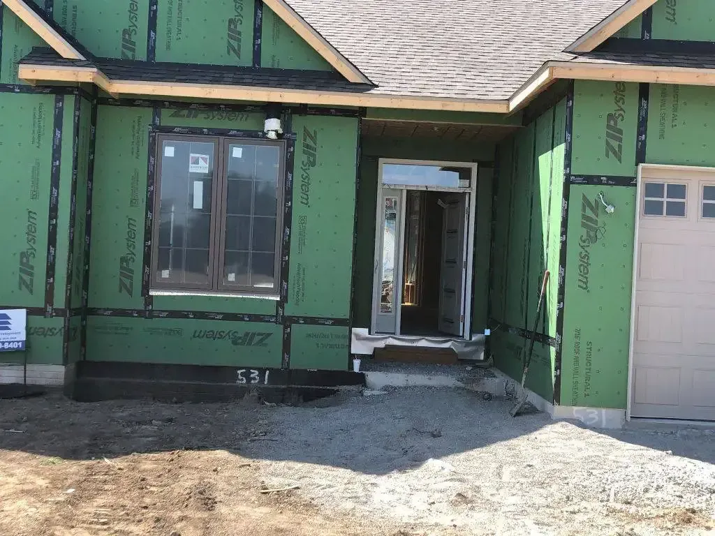 Green house exterior under construction with unfinished siding, front window, doorway, and garage door