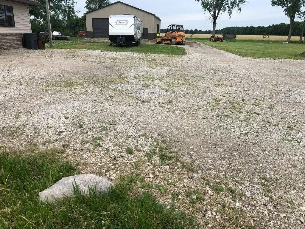 Gravel driveway leading to a white trailer and garage, with an orange tractor in the distance.