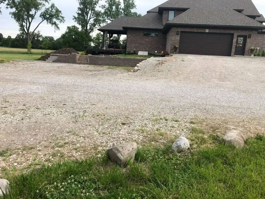 Large gravel driveway in front of a stone house with a garage and landscaped yard.