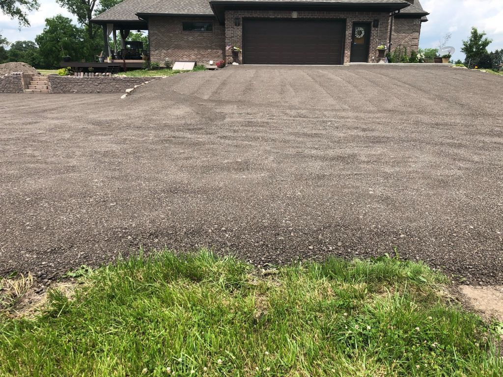 Wide gravel driveway leading to a brick house with a closed garage and green grass in the foreground