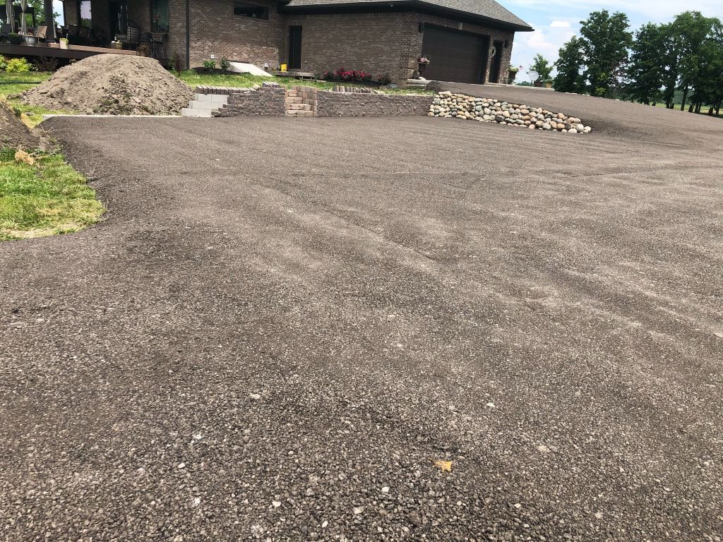 Gravel driveway leading to a brick house, with stone borders and green trees nearby