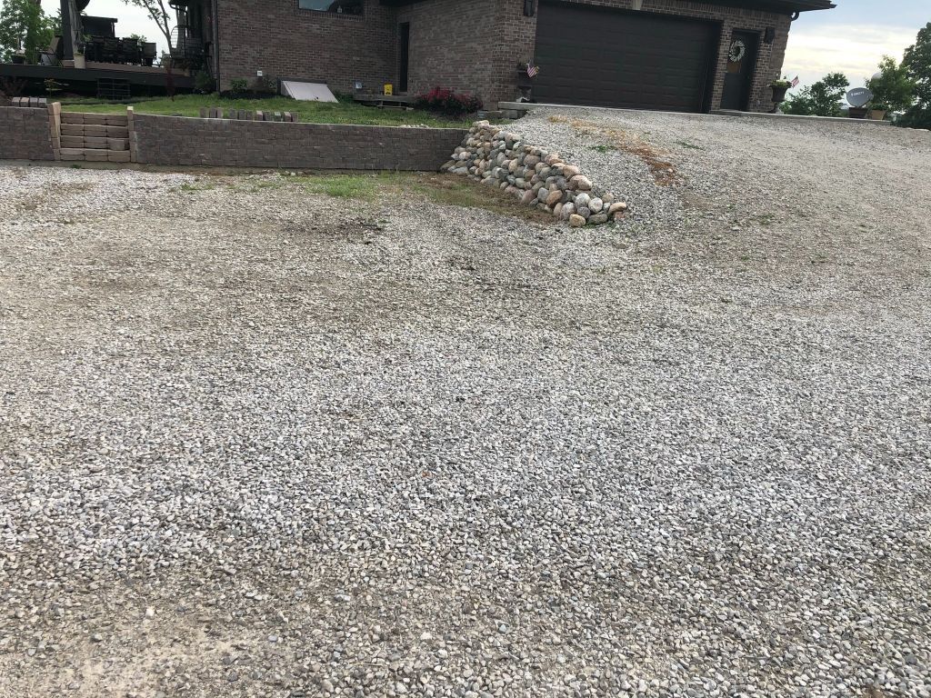 Gravel driveway leading to a brick house with garage and low stone retaining wall