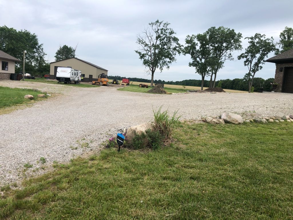 Gravel driveway and rural yard with trees, a white truck, and a small blue garden ornament in the foreground