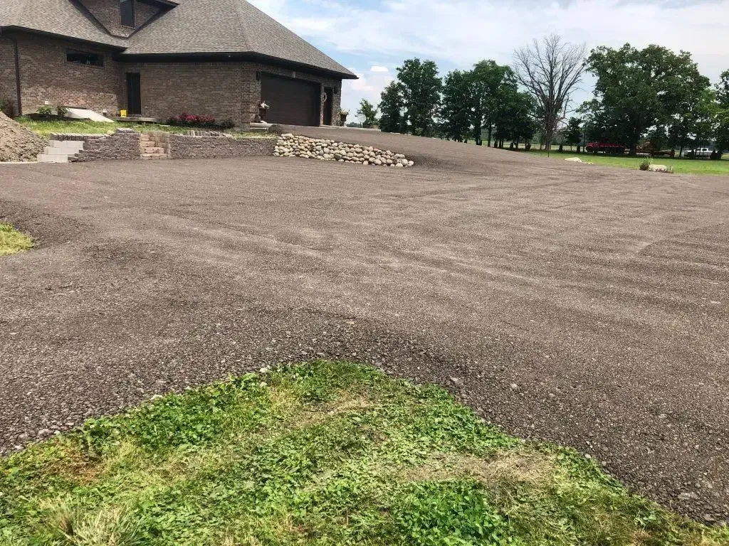 Gravel driveway beside a stone house with a grassy foreground and trees in the distance