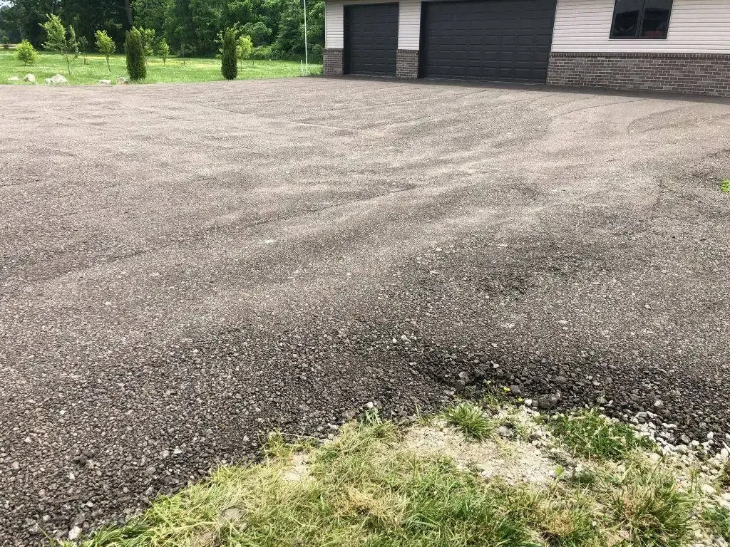 Gravel driveway beside a dark garage with trees and grass in the background