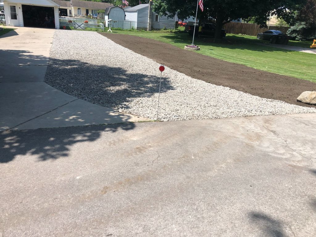 Driveway with a fresh white gravel section and a small red marker beside a house yard.