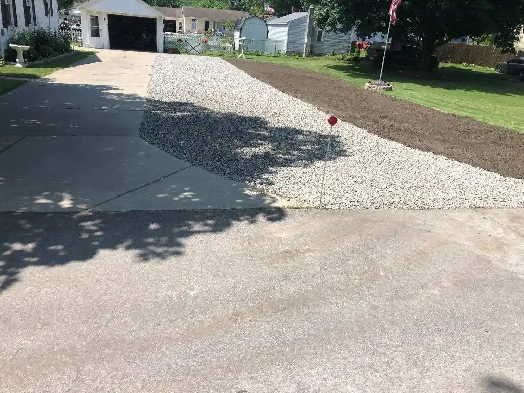 Driveway with fresh concrete and a white gravel strip beside a house, in bright daylight.