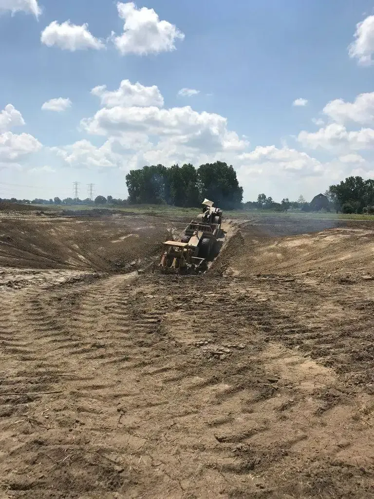 ATV rider driving through a muddy dirt field under a cloudy sky