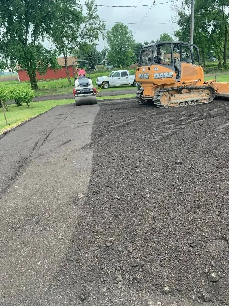 Roadwork scene with a skid steer leveling asphalt on a residential street behind a small car.