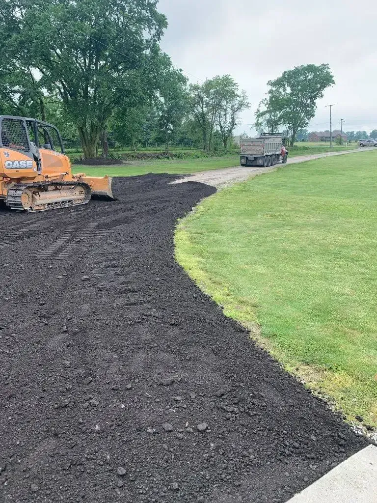 Orange bulldozer shaping a dark mulch path beside a green lawn in a park-like area