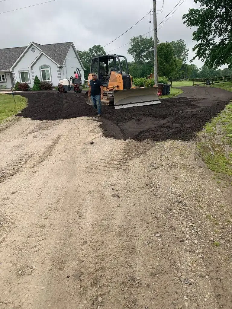 Workers and a skid steer spreading gravel on a driveway beside a house