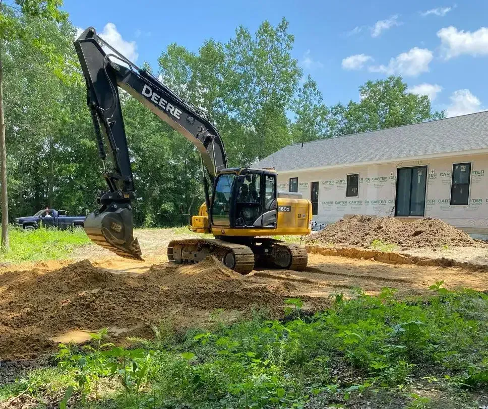 Yellow excavator moving dirt beside a house under construction on a sunny day