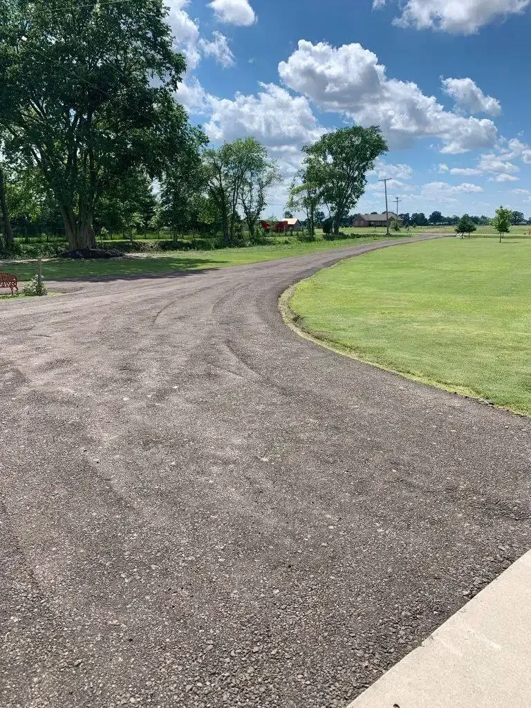 Curving gravel path through a green park under a bright, cloudy sky